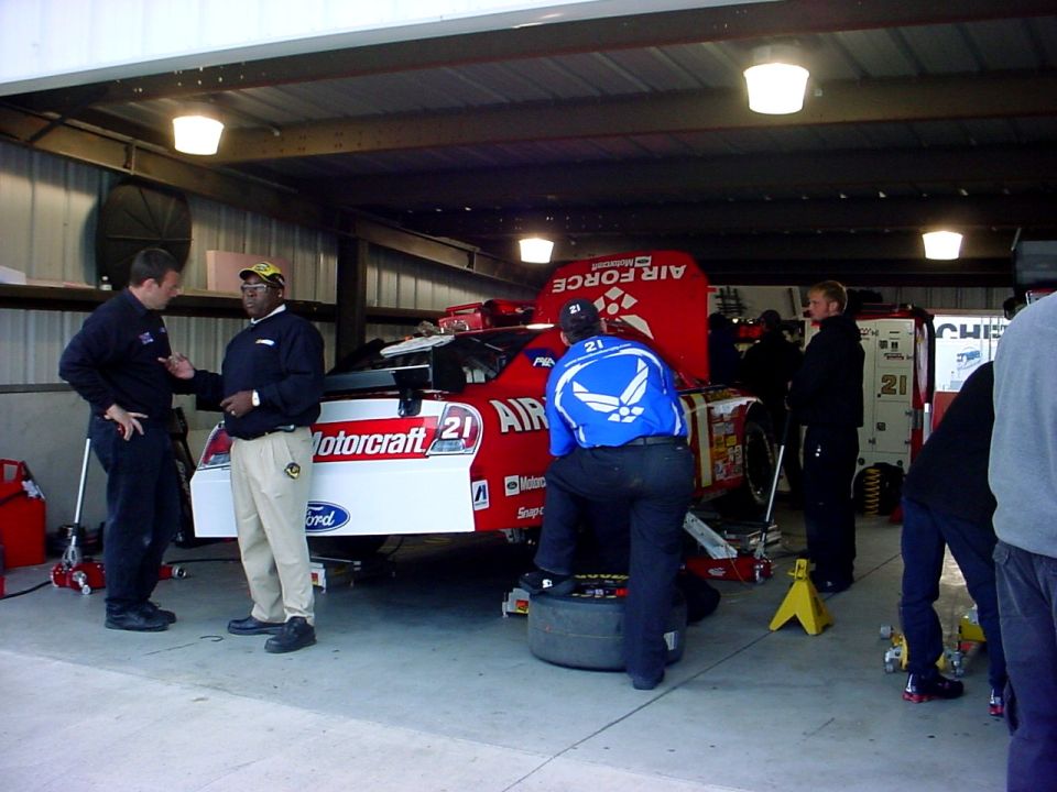 Race car in garage with crew members around it. One person is changing a tire