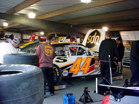 1993 Ford Mustang - Race car number 44 with UPS livery is being worked on in a garage, with other vehicles and tires visible.