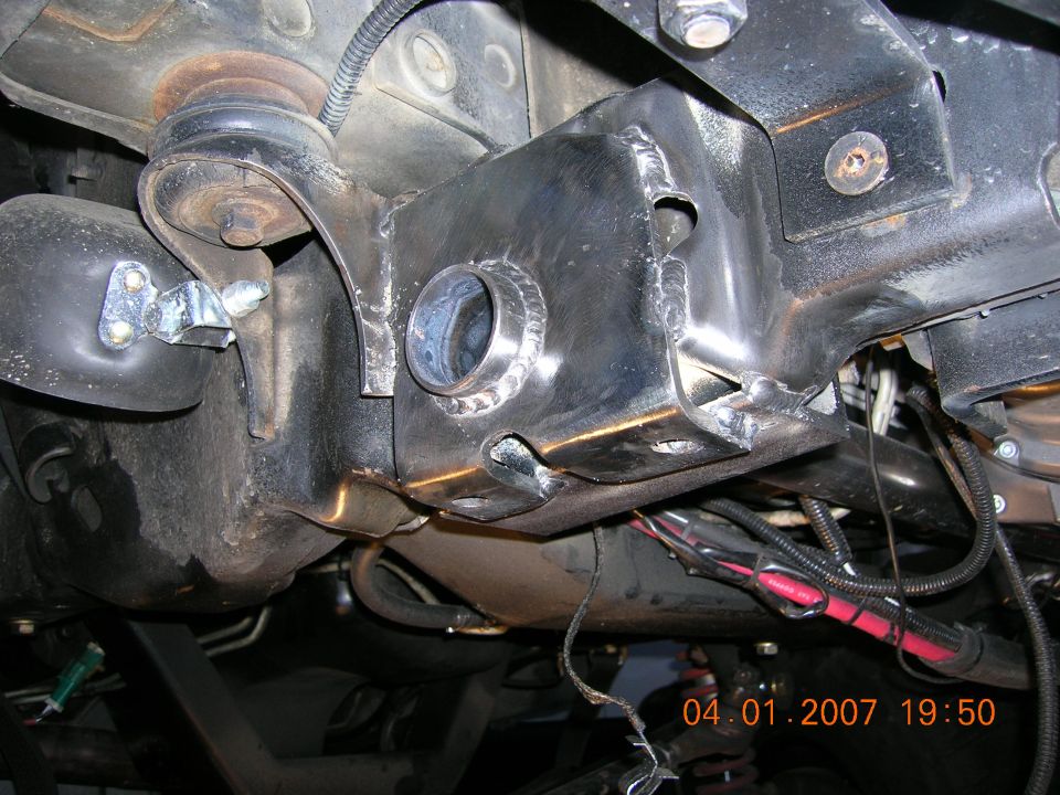 Freshly welded bare-steel suspension bracket with bushing bore on a truck frame rail underside