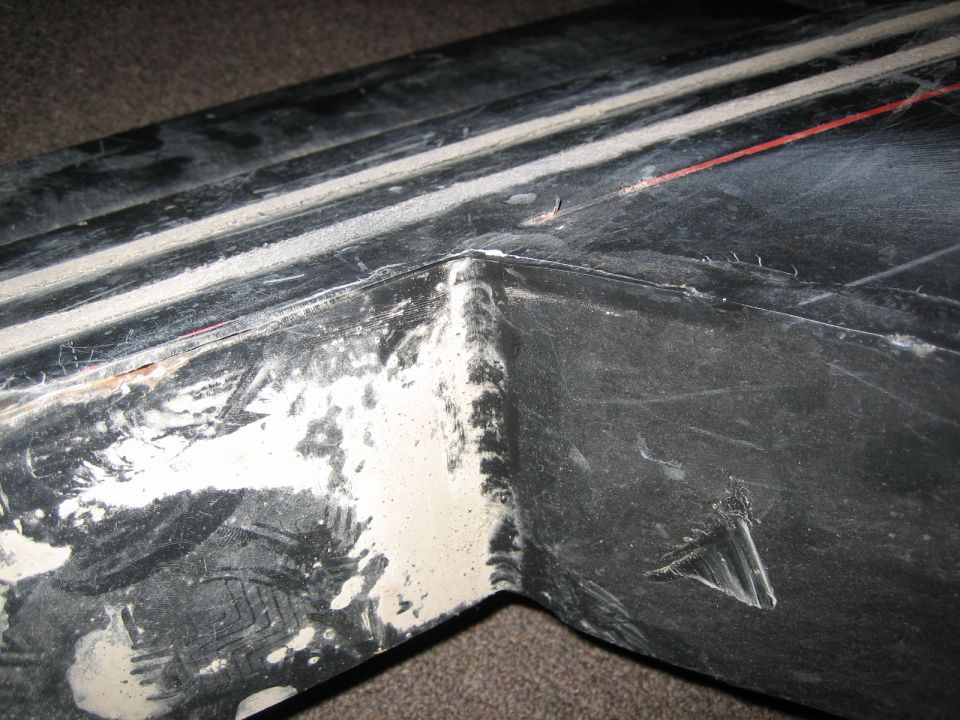 close-up of a damaged black plastic trim piece with white residue and a red line