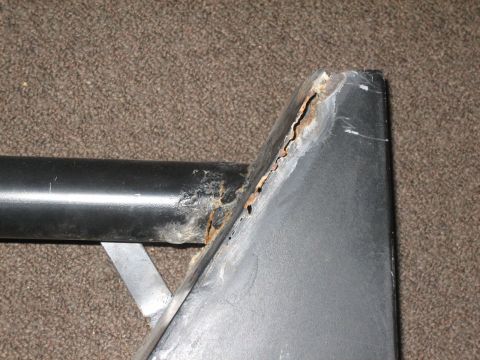 1995 Ford Bronco - A close-up view of a damaged and rusted metal component, likely a vehicle part, against a carpeted background.