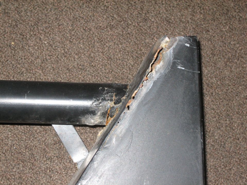 Close-up of heavily rusted metal corner with black pipe and silver bracket against carpet