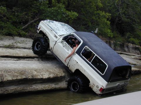 1996 Ford Bronco - This off-road SUV is navigating a difficult rocky terrain partially submerged in water.