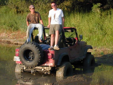 1996 Ford Bronco - This red Jeep Wrangler appears to be stuck in the mud with two people on it.