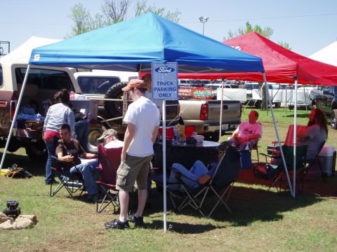 1978 Ford Bronco - A group of people relax under tents next to a 1978 Ford Bronco at an outdoor event.