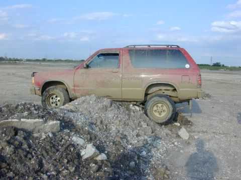 1996 Ford Bronco - A red SUV is stuck in the mud, with its front wheel on a pile of debris.