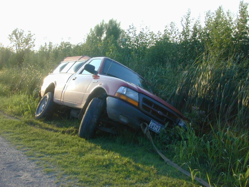 Red Ford Ranger pickup stuck nose-down in a ditch with recovery strap attached