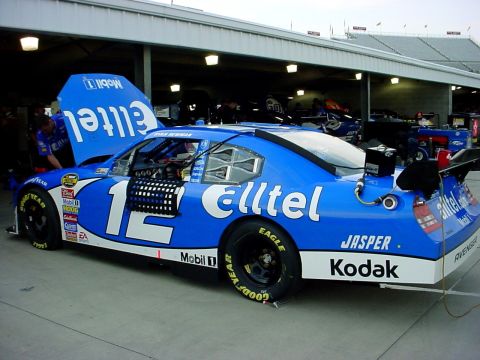 1993 Ford Mustang - A blue NASCAR race car with "elltel" sponsorship is parked in a pit stall with its hood up.