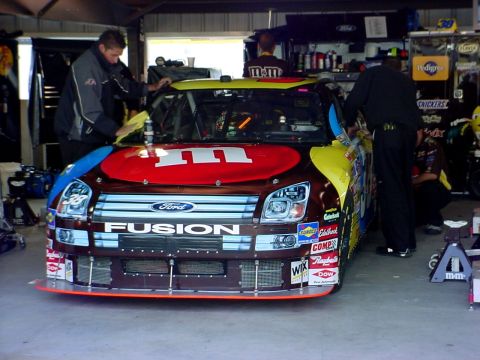 1993 Ford Mustang - A Ford Fusion race car with M&M's livery is being worked on in a garage.