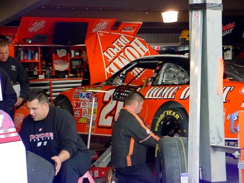 1993 Ford Mustang - Race car undergoing service in the pit area, with crew members attending to the vehicle.