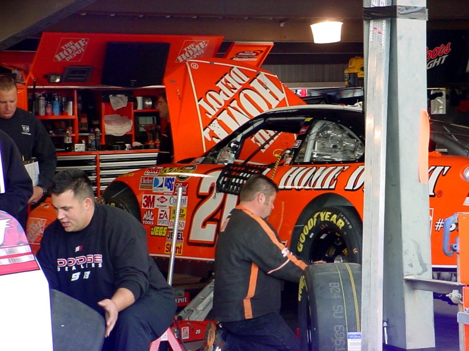 NASCAR pit crew working on a race car in a garage, with "The Home Depot" logos visible
