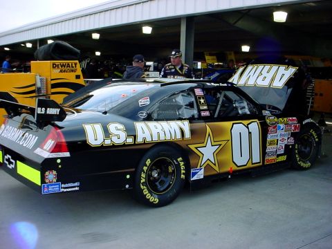 1993 Ford Mustang - Stock car with U.S. Army livery and sponsor decals is parked in a garage.