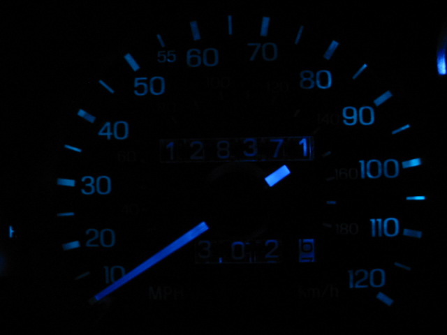 Car dashboard with blue illuminated speedometer and odometer showing 128371 miles