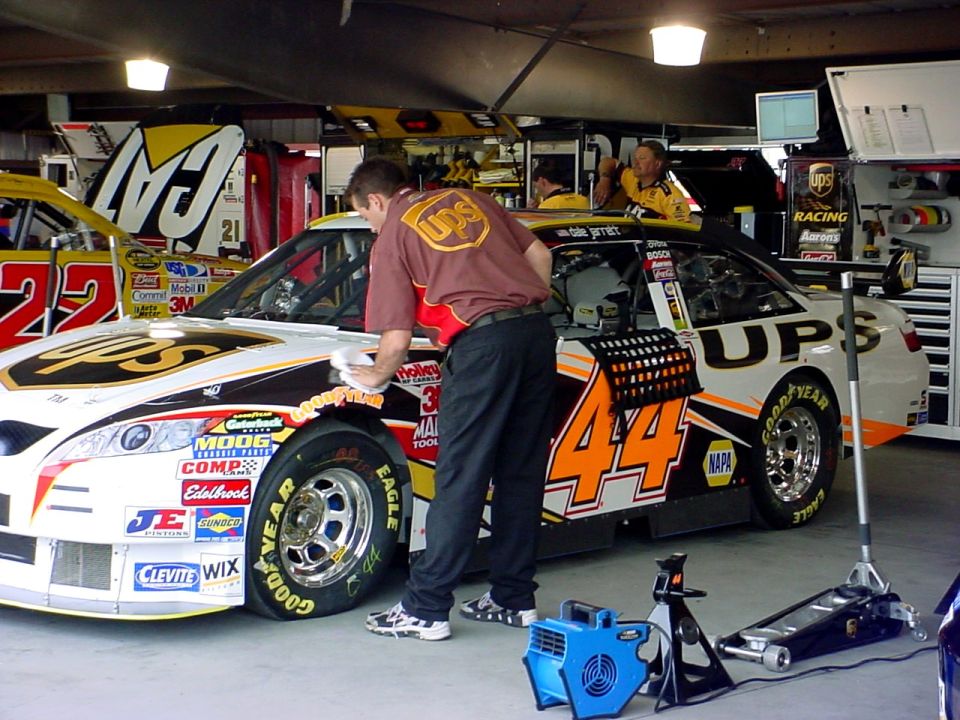 Guy wiping down a race car with number 44 and UPS logos. Another car with number 22 is visible
