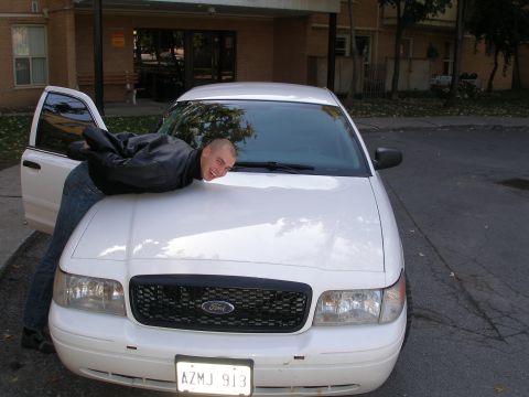 2003 Ford Crown Victoria - A man poses humorously on the hood of a white 2003 Ford Crown Victoria.