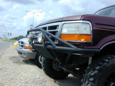 1996 Ford Bronco - A close-up of a modified Ford F-Series truck's front end, parked alongside another vehicle on a roadside.