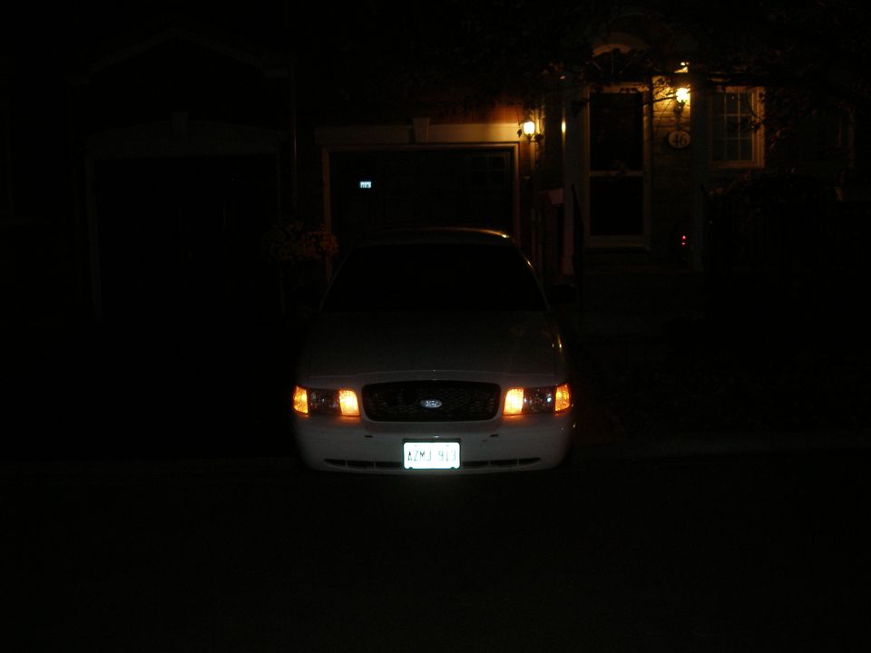 White Ford sedan front view at night with parking lights on in a driveway