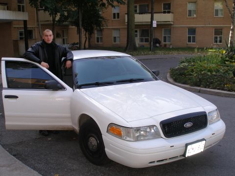 2003 Ford Crown Victoria - A man poses next to a white Ford Crown Victoria, showing its front grille and open driver's side door.