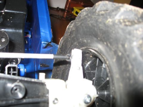 1990 Ford Bronco - A screwdriver is used to adjust a component near the wheel of a blue remote control car.