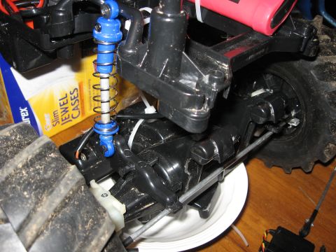 1990 Ford Bronco - Close-up of an RC car's suspension system and chassis components, with a jewel case box in the background.