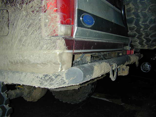 Mud-covered rear tailgate and tube bumper of a Ford truck at night with spare tire mounted above