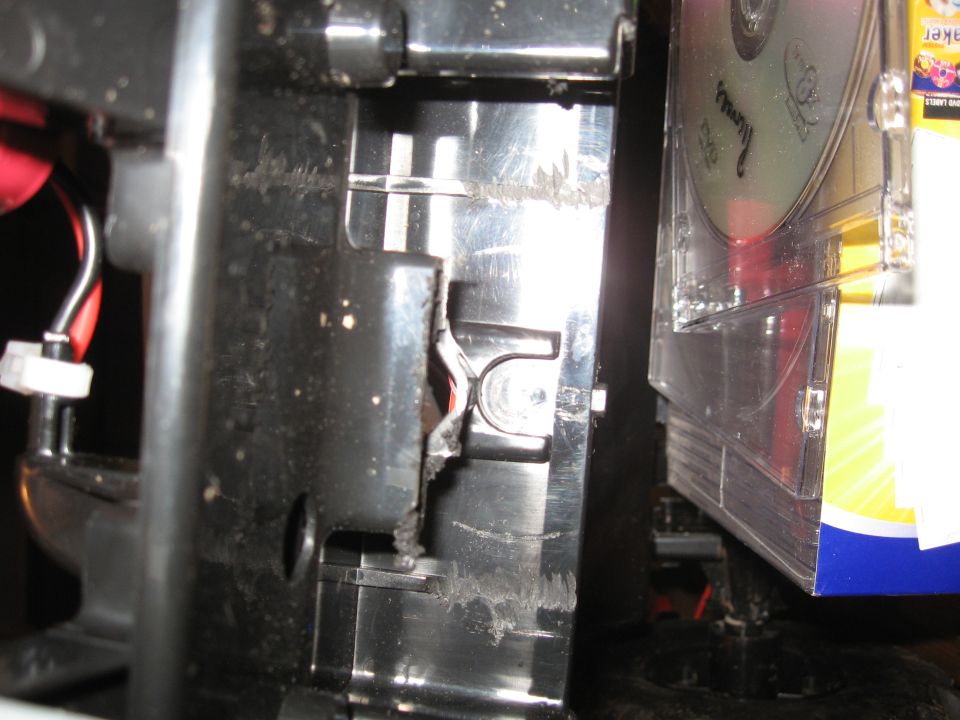 Close-up of damaged black plastic housing with exposed wires and a stack of CDs to the right