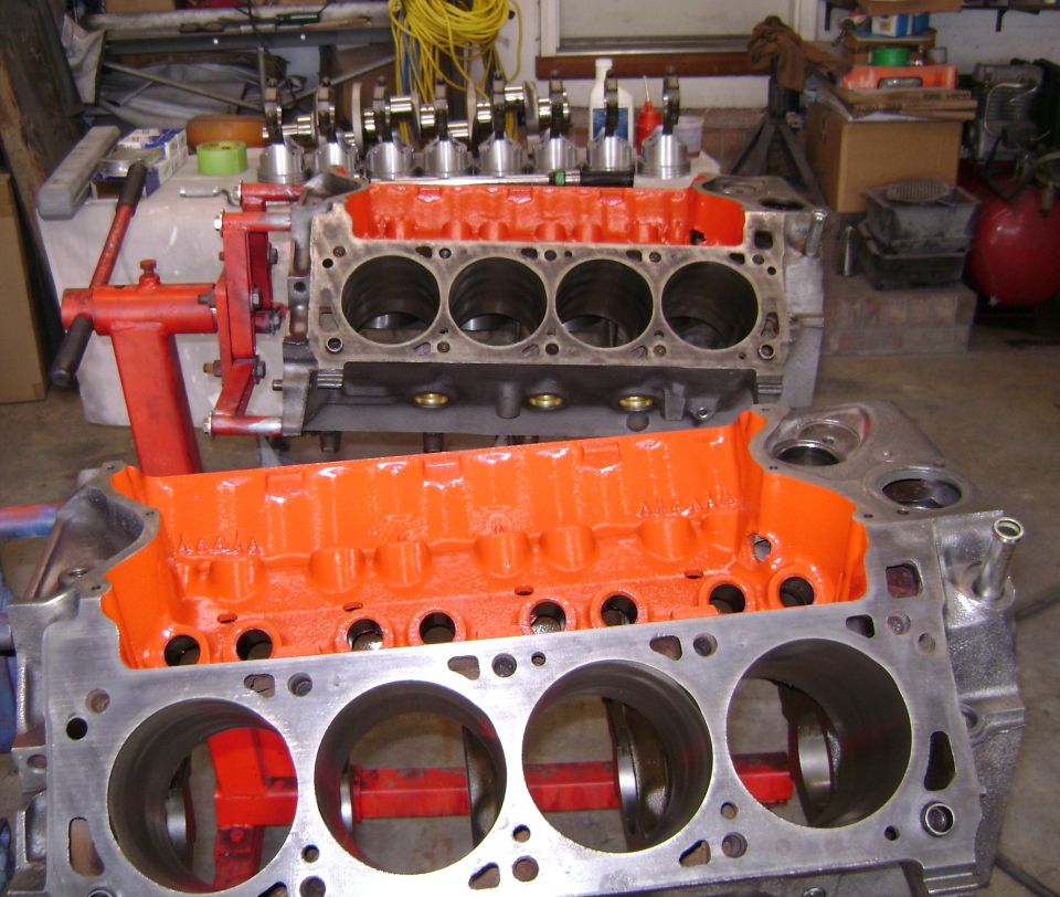 Two V8 engine blocks with orange-painted valleys during rebuild in a garage
