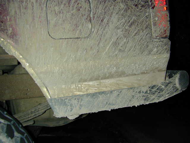 Rear quarter panel, fuel door and bumper of a truck caked in dried mud at night
