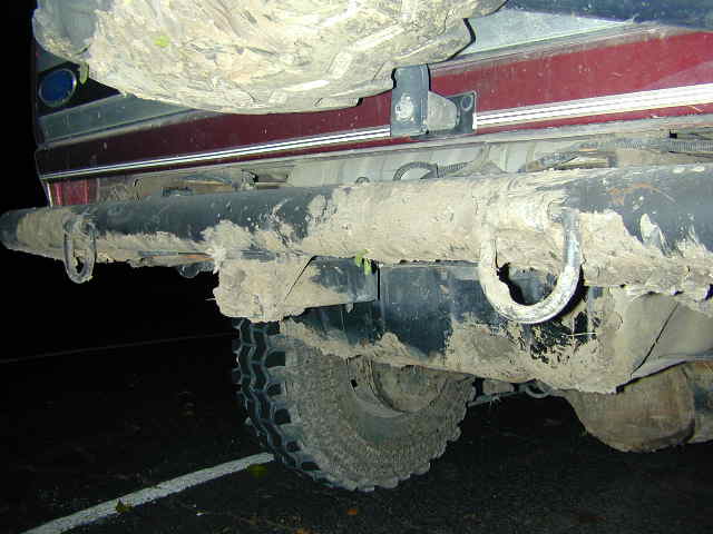 Mud-caked rear bumper and off-road tire of maroon SUV at night