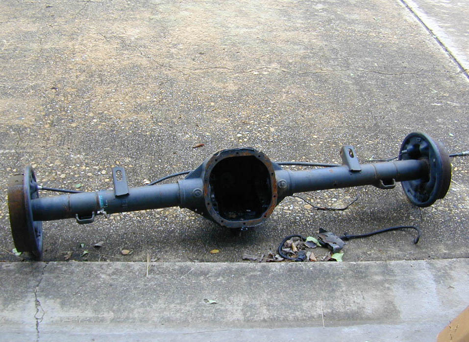Bare rear axle housing on concrete with differential cover removed and backing plates attached