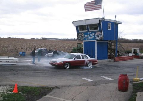 1998 Ford Crown Victoria - A two-tone 1998 Ford Crown Victoria performs a burnout in front of a drag strip tower.