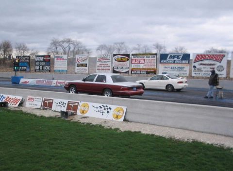 1998 Ford Crown Victoria - Two cars are lined up on a drag strip, ready for a race.