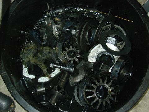 1996 Ford Bronco - A collection of greasy differential components and rags are piled inside a black container.
