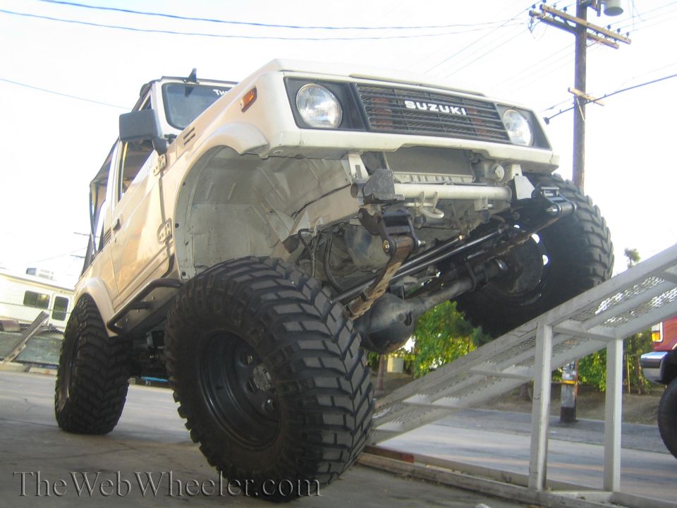 Lifted tan Suzuki Samurai on big mud tires, front bumper removed, exposed axle