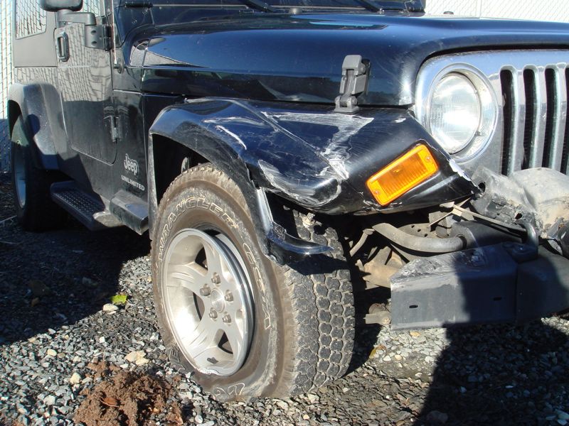 Front corner of a black Jeep Wrangler with a dented fender and flat tire