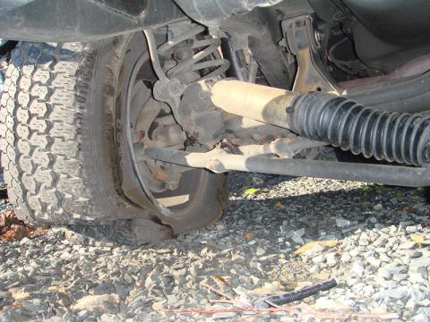 1996 Ford Bronco - Close-up view of a vehicle's undercarriage, showing a flat tire and suspension system.