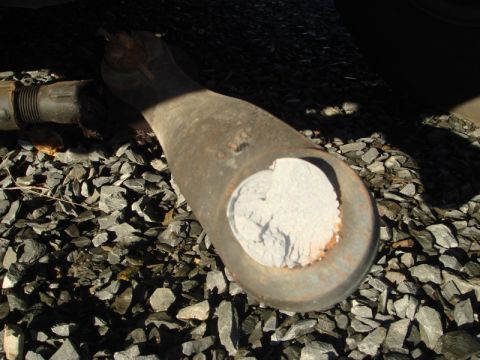 1996 Ford Bronco - A close-up view of a corroded metal part lying on gravel, showing significant wear.
