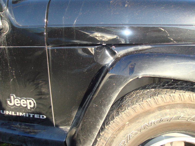 Black Jeep Wrangler Unlimited with dented fender and door panel