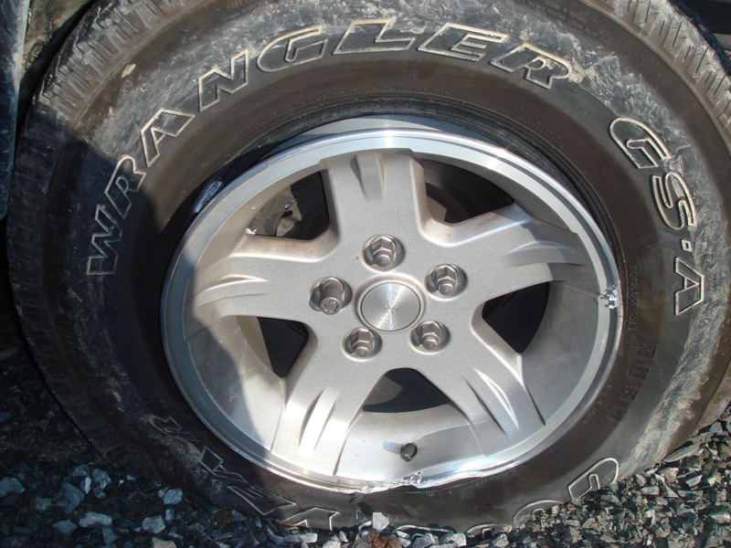 Silver five-spoke wheel with a flat tire showing "Wrangler GSA" text