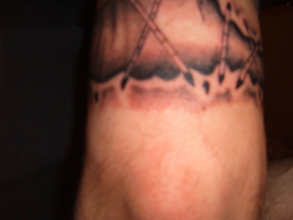 Close-up of a tattoo on an arm, showing a dark, abstract design with some red discoloration below it