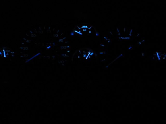 Car dashboard with blue illuminated gauges, including speedometer, tachometer, fuel, and temperature
