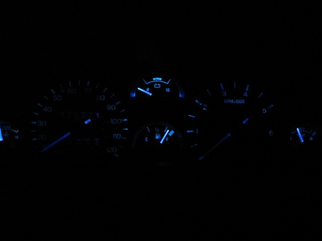 Car dashboard with blue illuminated gauges, including speedometer, tachometer, and fuel gauge