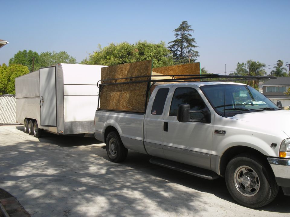 White Ford Super Duty pickup with bed racks towing an enclosed trailer