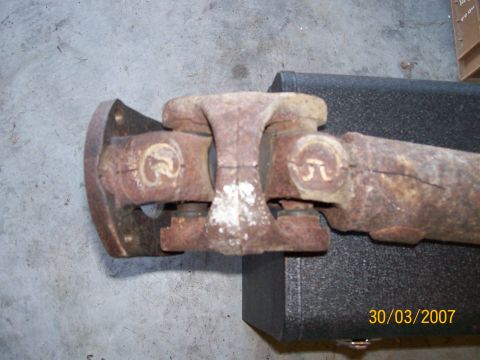 1996 Ford Bronco - Close-up of a rusty driveshaft with universal joints and a flange, resting on a black surface.
