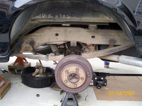 1996 Ford Bronco - Rear axle and suspension components of a black 1996 Ford Bronco, with the brake drum removed and vehicle supported by jack stands.