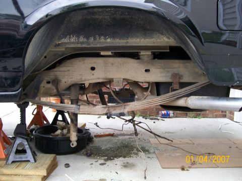 1996 Ford Bronco - The underside of a vehicle is shown with its rear suspension components exposed and undergoing maintenance.
