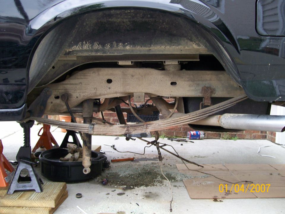 rear leaf springs, shock, and exhaust pipe on a vehicle supported by jack stands