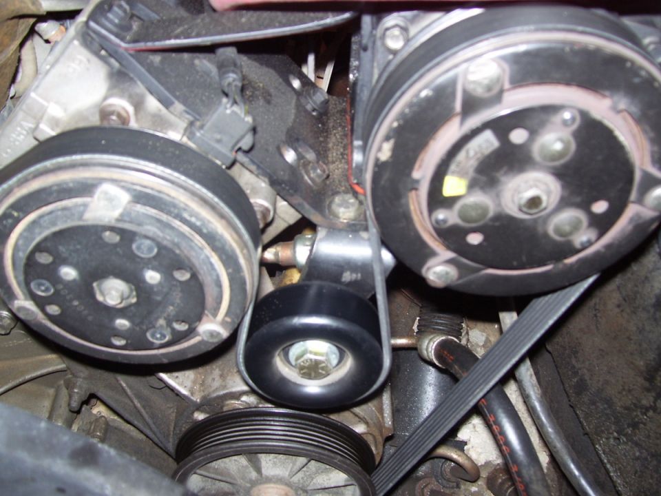 Engine bay close-up of two compressor clutch pulleys, idler pulley and serpentine belt