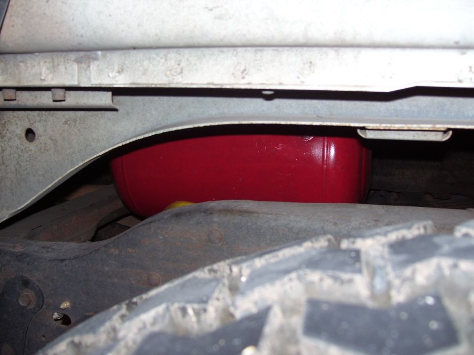 Underside of vehicle showing a red fuel tank or similar component near the tire