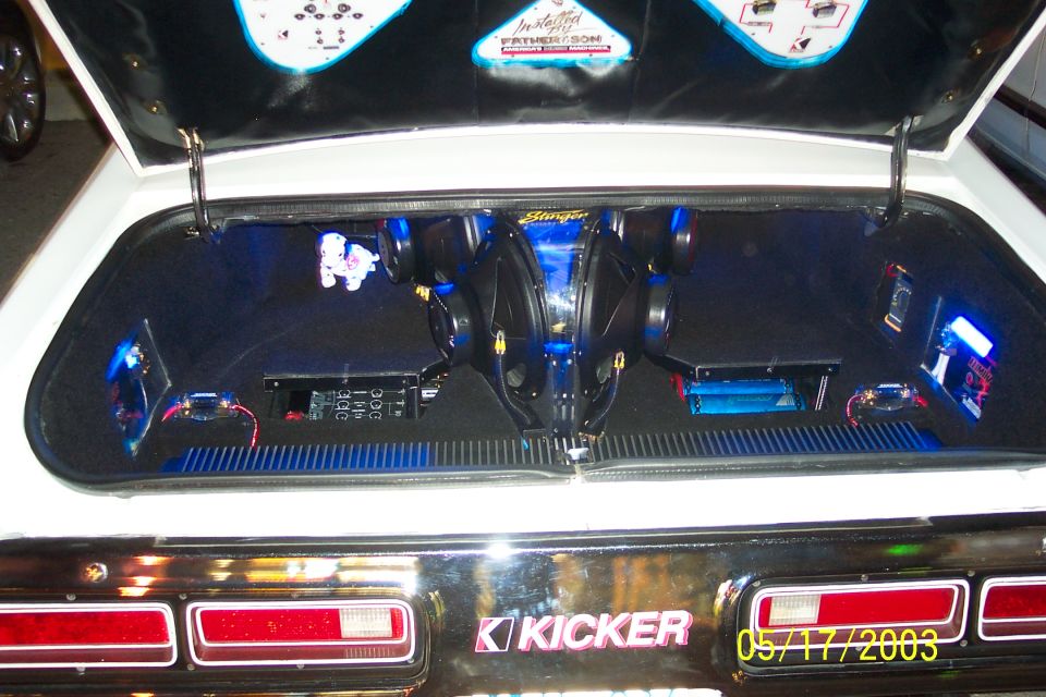 Car trunk interior with two subwoofers, amplifiers, and blue LED lighting. Kicker logo visible on the trunk lid